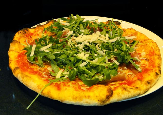 Pizza al crudo <small>((tomate, mozzarella, jamón serrano, rúcula, virutas de parmigiano, aceite y orégano)</small>